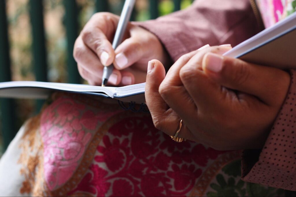 A woman’s hands writing thoughts in a personal journal notebook.
