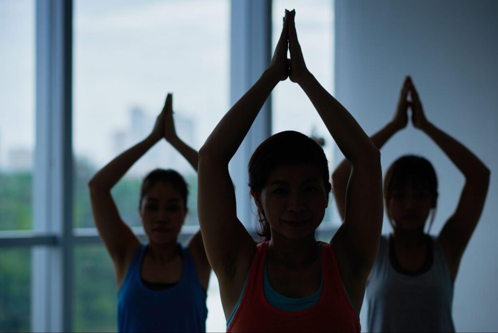 Three yoga practitioners posing with their arms stretched over their heads.