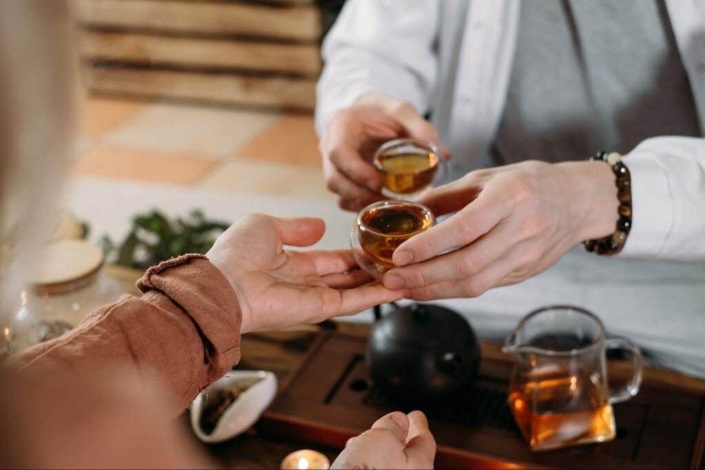 A person handing a cup of tea to another person during a Chinese tea ceremony.