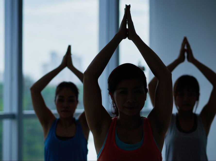 Three yoga practitioners posing with their arms stretched over their heads.