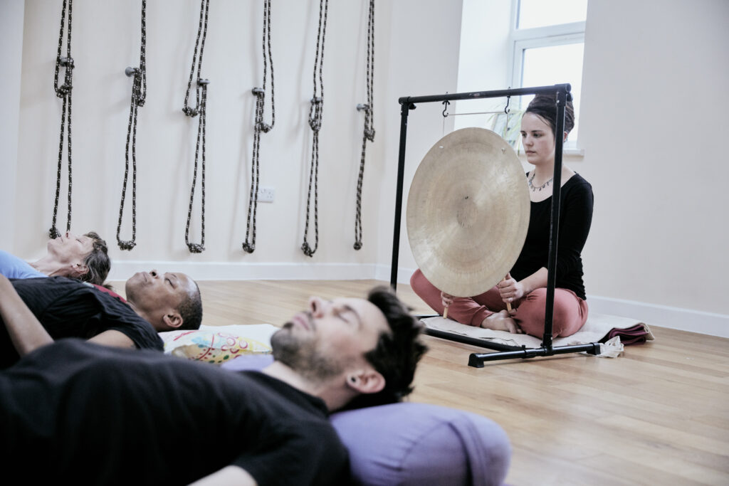 A woman prepares to use a gong to provide a sound bath to participants.