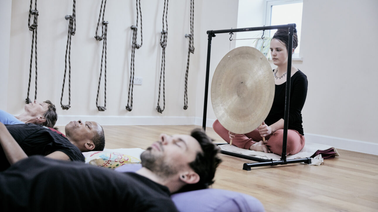 A woman prepares to use a gong to provide a sound bath to participants.