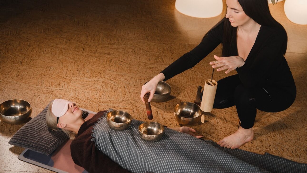 A woman lying in a calming room, blindfolded, undergoing a sound bath.