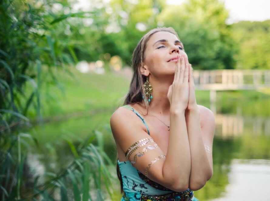 Woman standing in green nature at sunset, praying quietly and embracing spiritual reflection.
