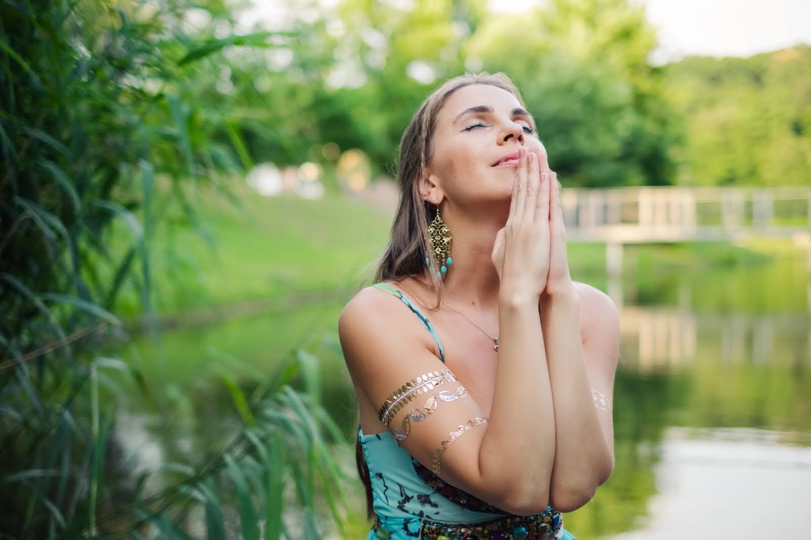 Woman standing in green nature at sunset, praying quietly and embracing spiritual reflection.