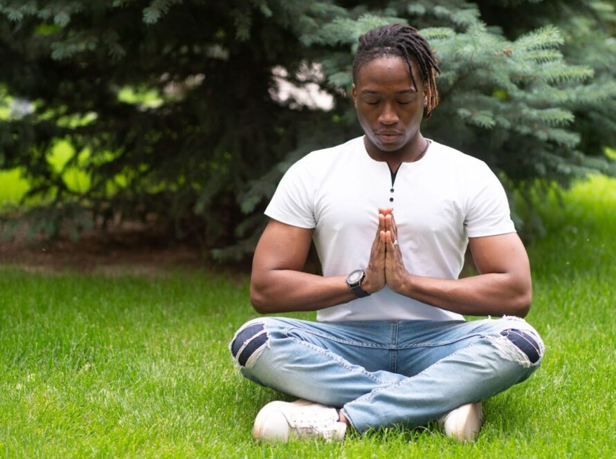 A man meditating in a seated yoga pose on a green park lawn.