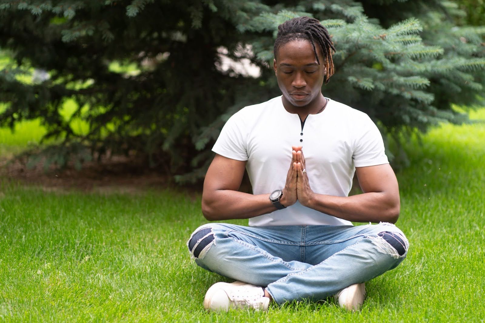 A man meditating in a seated yoga pose on a green park lawn.