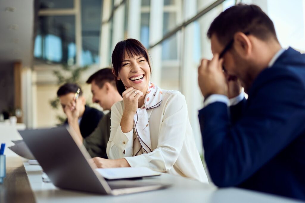 A lady executive shares a laugh with colleagues, maintaining emotional balance during a demanding team meeting.