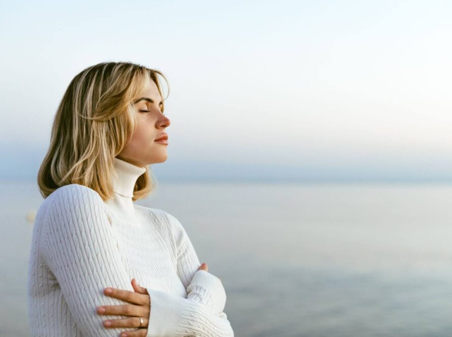 Beautiful woman in a sweater practicing mindful meditation on a calm seaside shoreline.