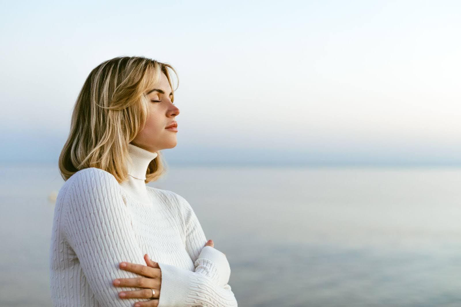 Beautiful woman in a sweater practicing mindful meditation on a calm seaside shoreline.