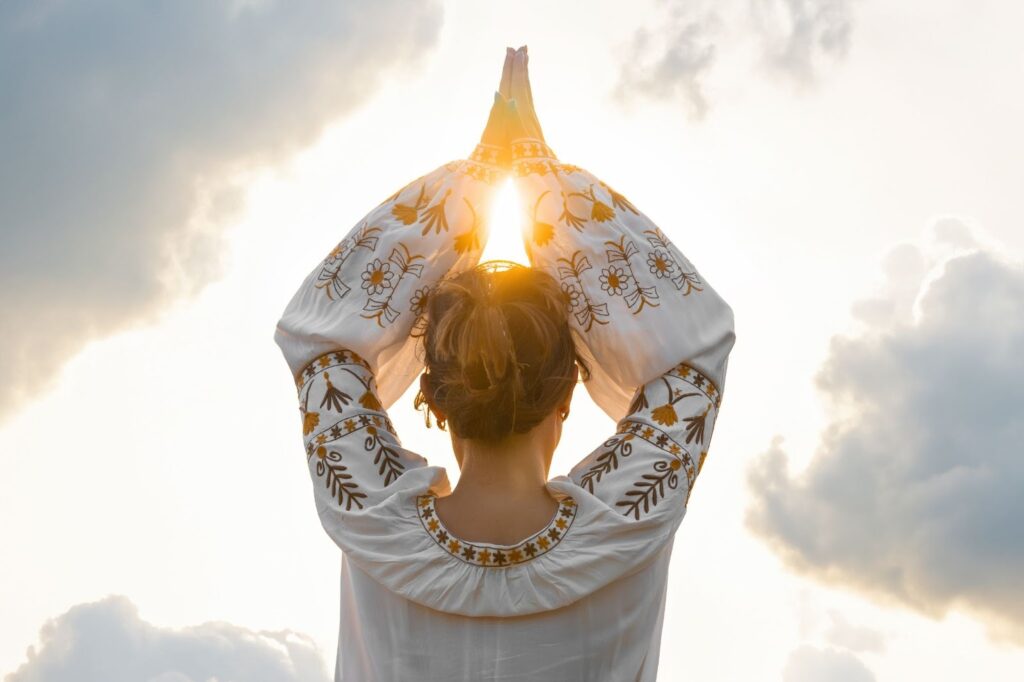 Rear view of a female figure in prayer with hands together, symbolizing gratitude and spiritual energy.