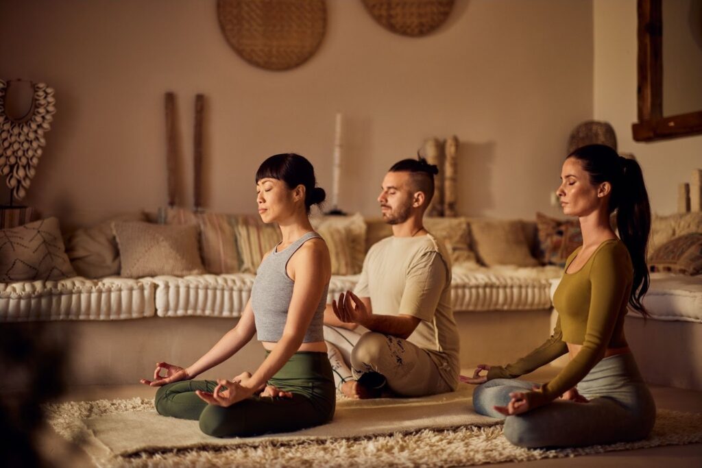 Three people engaged in a seated meditation practice with eyes closed.