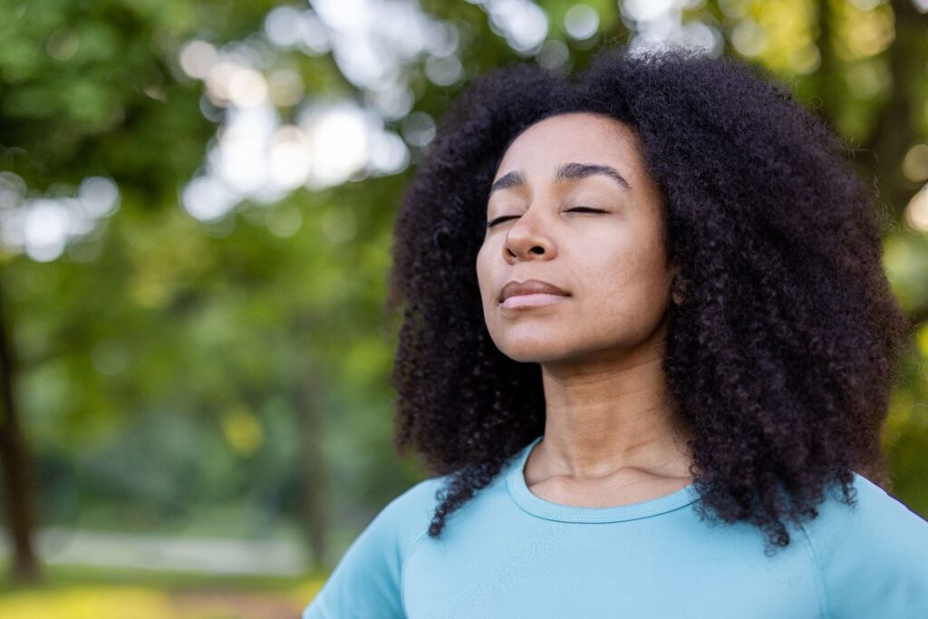 Woman practicing mindfulness outdoors with eyes closed in a serene natural setting.