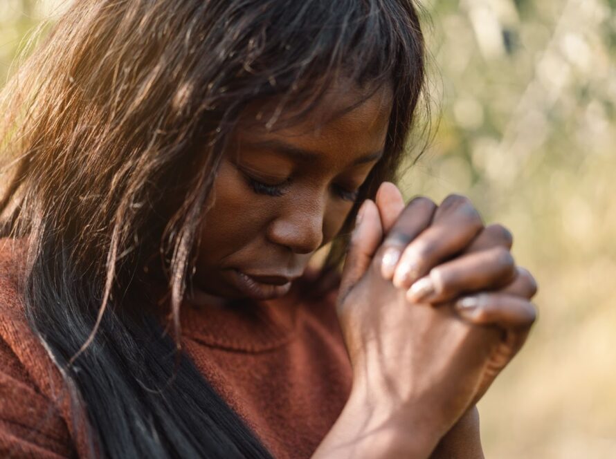 A Black woman standing outdoors in focused prayer, expressing faith and devotion