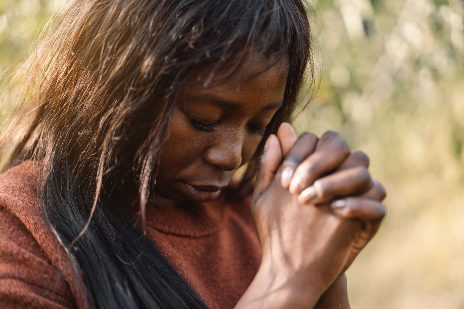 A Black woman standing outdoors in focused prayer, expressing faith and devotion