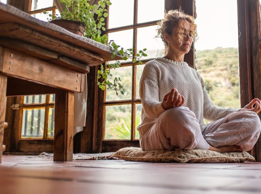 Woman with her eyes closed and her legs crossed next to a table and an open door. 