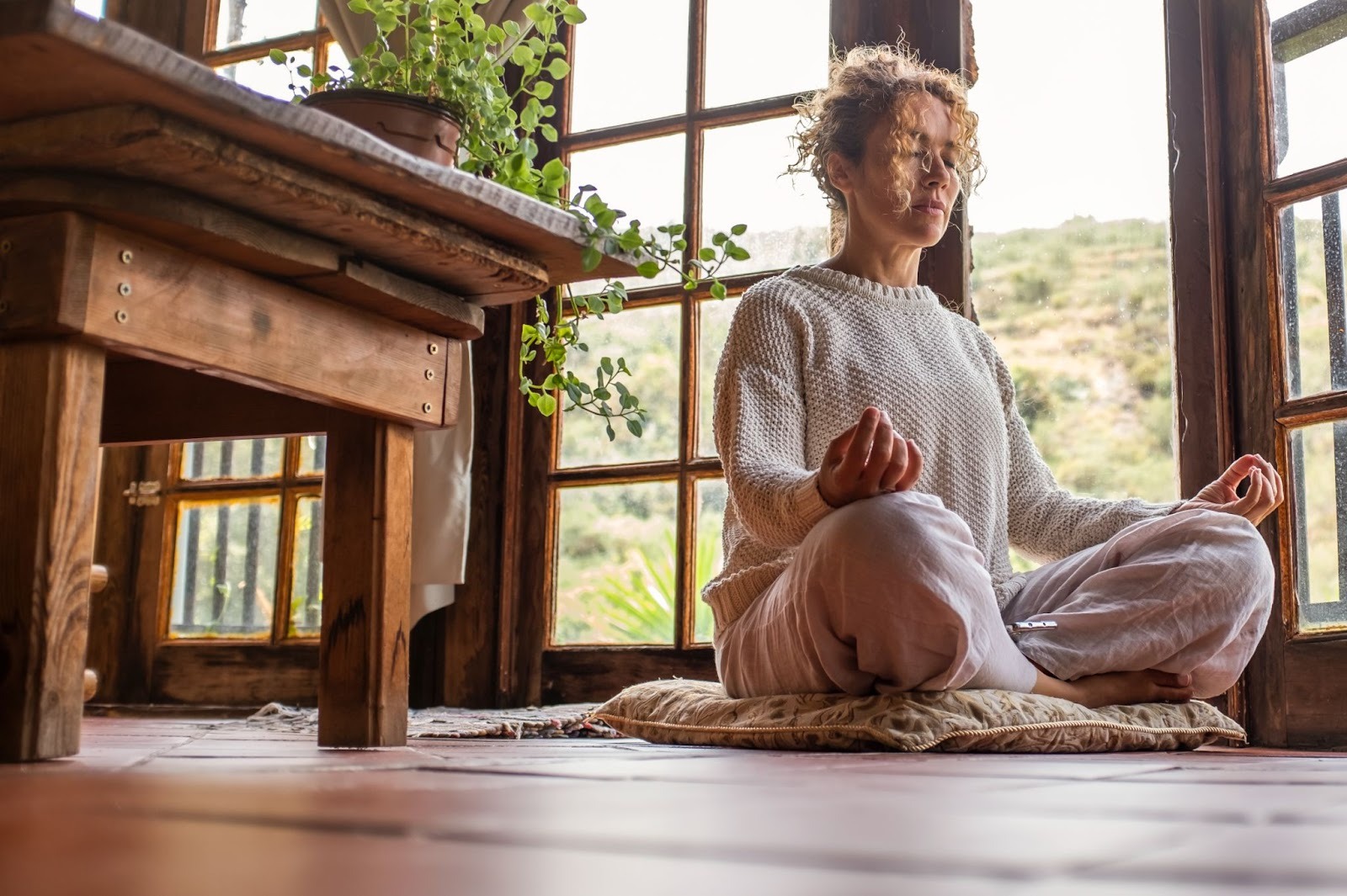 Woman with her eyes closed and her legs crossed next to a table and an open door. 