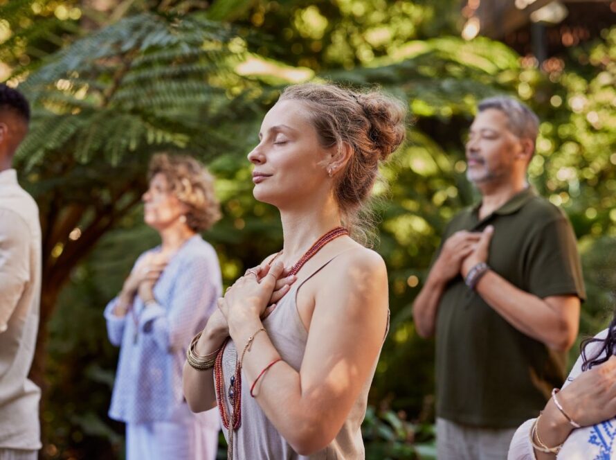 Diverse community gathered outdoors, standing in reflective meditation amid lush greenery