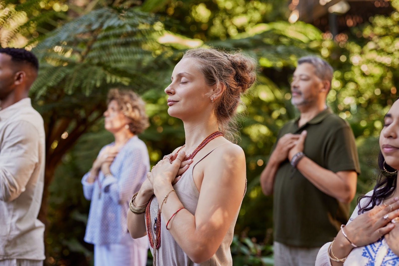 Diverse community gathered outdoors, standing in reflective meditation amid lush greenery