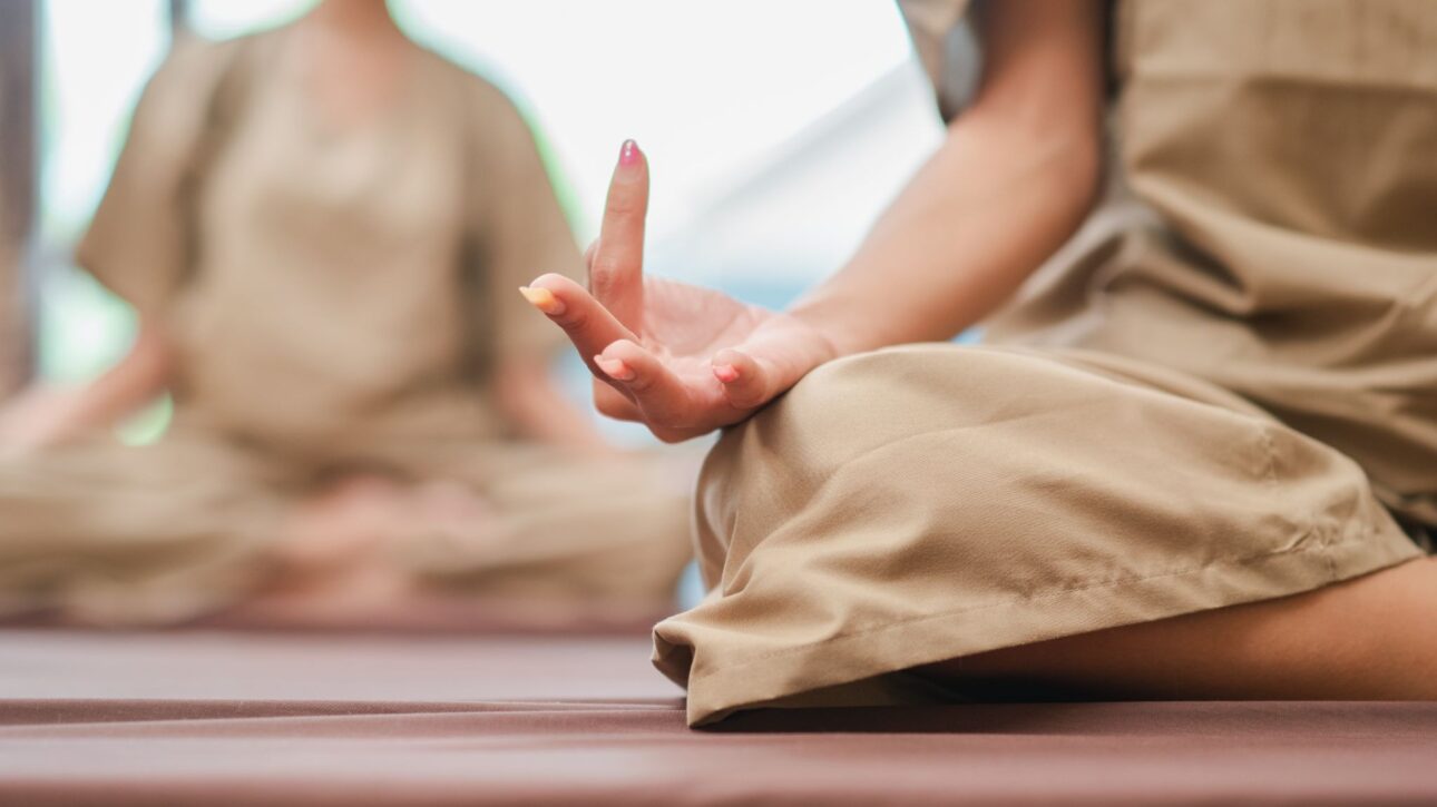 Cropped shot of two women seated with hands in a mudra pose, practicing meditation techniques