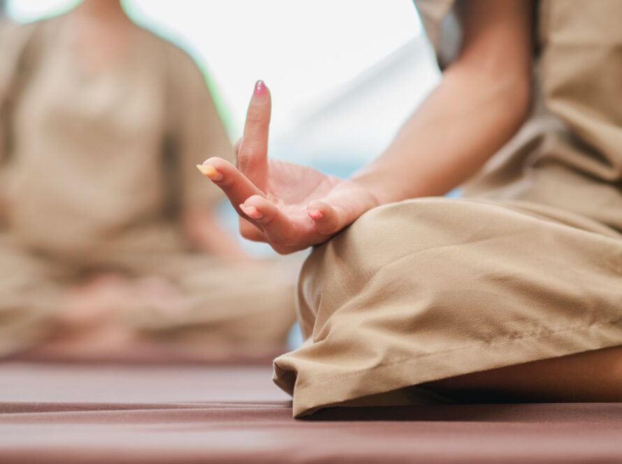Cropped shot of two women seated with hands in a mudra pose, practicing meditation techniques
